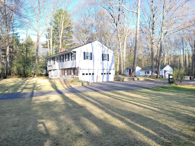 view of side of property featuring a garage, a chimney, a yard, and aphalt driveway