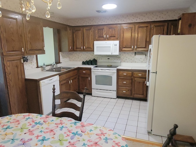 kitchen with a sink, white appliances, light countertops, brown cabinetry, and light tile patterned floors