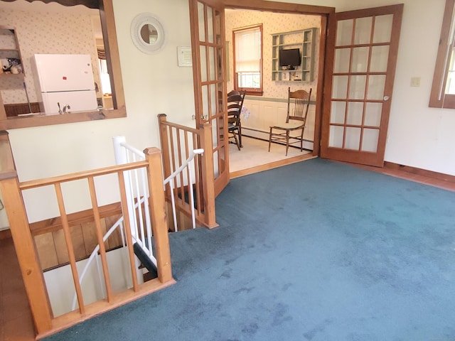 carpeted empty room with wallpapered walls, french doors, and a baseboard heating unit