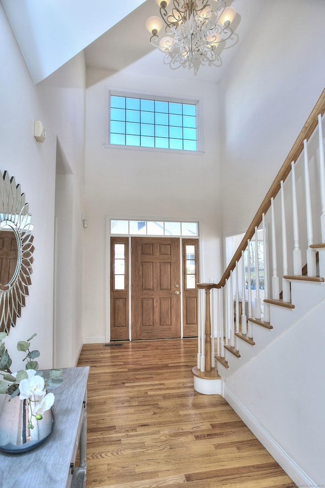 foyer entrance featuring baseboards, a notable chandelier, light wood-style floors, a high ceiling, and stairs