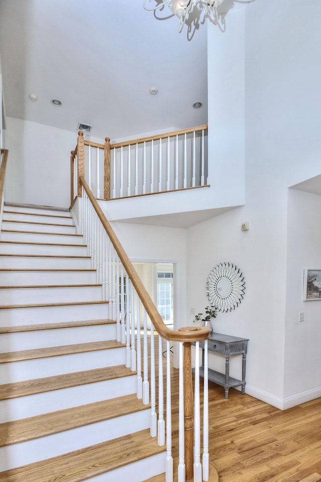 stairs featuring a high ceiling, a notable chandelier, recessed lighting, baseboards, and wood finished floors