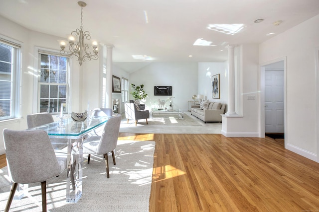 dining area featuring plenty of natural light, decorative columns, light wood-type flooring, and a chandelier