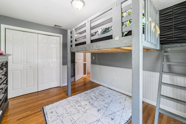 unfurnished bedroom featuring a closet, wainscoting, wood finished floors, and visible vents