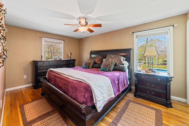 bedroom featuring ceiling fan, baseboards, multiple windows, and wood finished floors