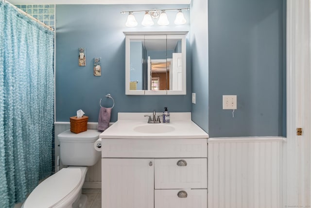 bathroom with vanity, toilet, a shower with curtain, and a wainscoted wall