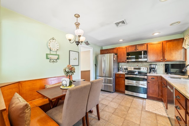 kitchen featuring a notable chandelier, appliances with stainless steel finishes, brown cabinetry, backsplash, and visible vents