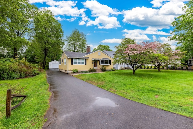 bungalow-style home featuring a chimney, a front yard, an outdoor structure, and a detached garage