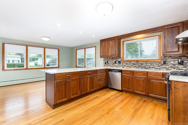 kitchen featuring a sink, a peninsula, appliances with stainless steel finishes, a baseboard radiator, and light wood-style floors