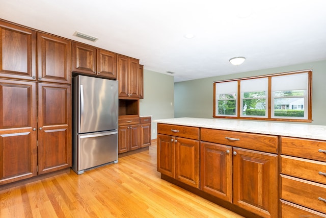 kitchen featuring freestanding refrigerator, brown cabinets, light wood finished floors, and visible vents