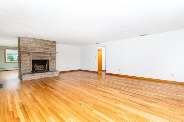 unfurnished living room with light wood-type flooring, visible vents, a baseboard radiator, baseboards, and a stone fireplace