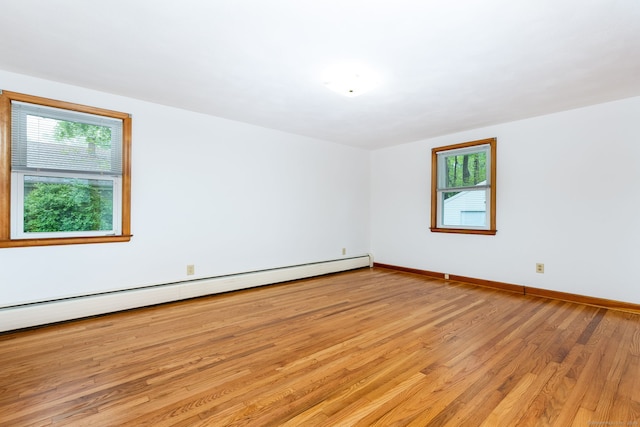 empty room with plenty of natural light, baseboards, a baseboard heating unit, and light wood-style floors