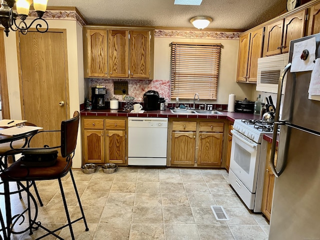 kitchen featuring a textured ceiling, white appliances, visible vents, a sink, and tile counters