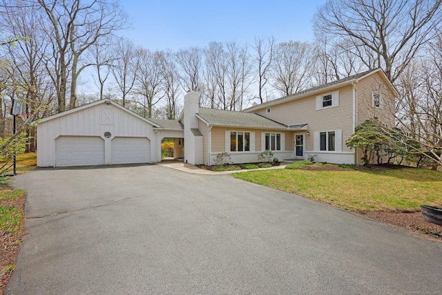 traditional-style home featuring aphalt driveway, a front yard, a chimney, brick siding, and an attached garage