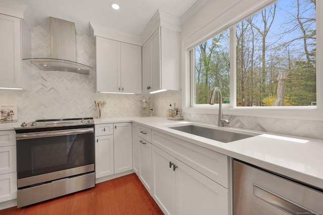kitchen with a sink, light countertops, wall chimney exhaust hood, stainless steel appliances, and decorative backsplash