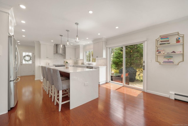 kitchen with freestanding refrigerator, wall chimney range hood, light countertops, tasteful backsplash, and light wood-style flooring
