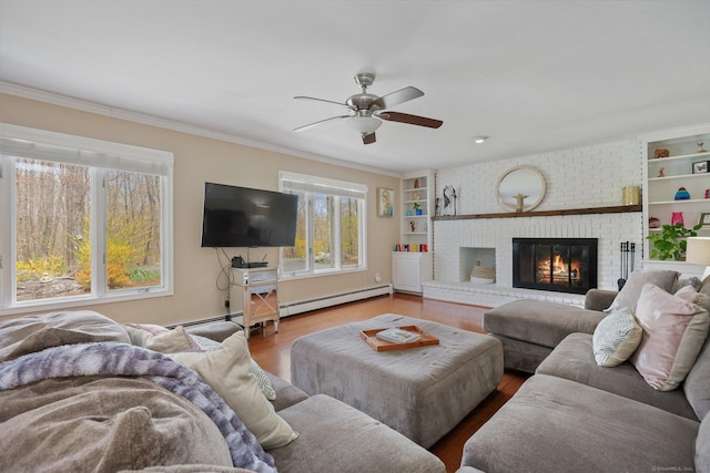 living area with a ceiling fan, crown molding, a brick fireplace, wood finished floors, and a baseboard radiator