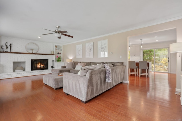living room featuring ornamental molding, a brick fireplace, wood finished floors, ceiling fan, and recessed lighting
