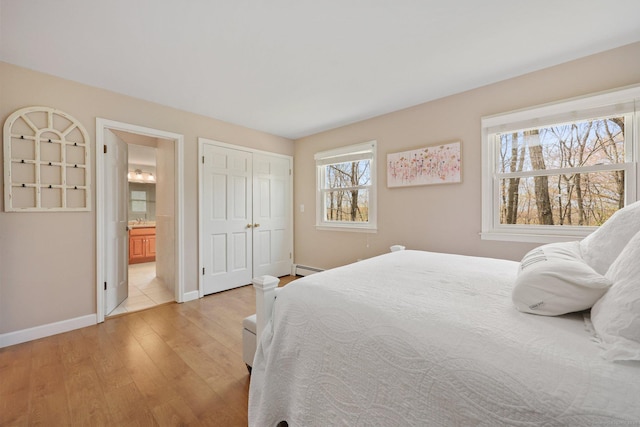 bedroom featuring baseboards, a baseboard heating unit, a closet, light wood-style floors, and ensuite bathroom