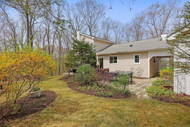exterior space with a shingled roof, a patio, a chimney, and a yard