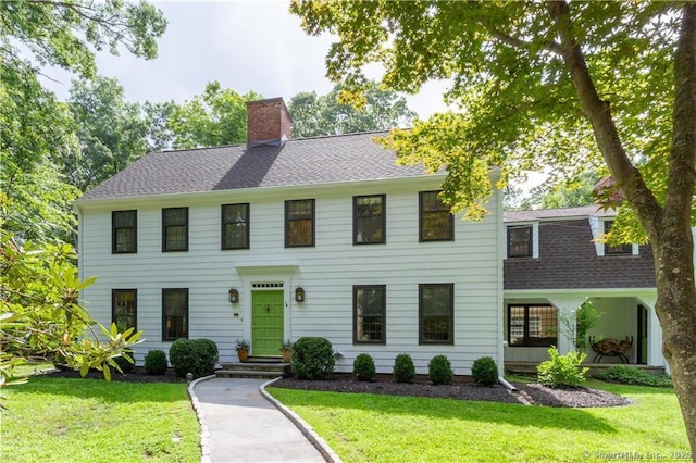 colonial home with a chimney, a shingled roof, and a front yard