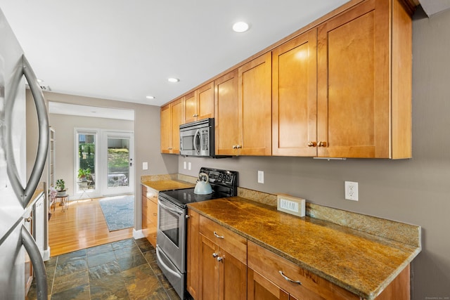 kitchen with stone finish floor, brown cabinets, baseboards, stainless steel appliances, and recessed lighting