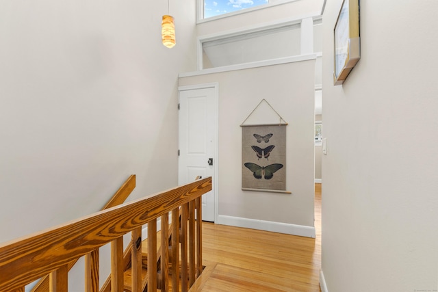 corridor with light wood-type flooring, baseboards, and an upstairs landing