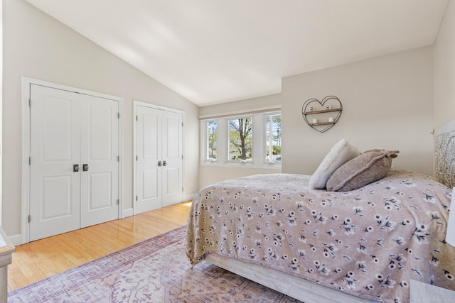 bedroom with multiple closets, vaulted ceiling, and wood finished floors