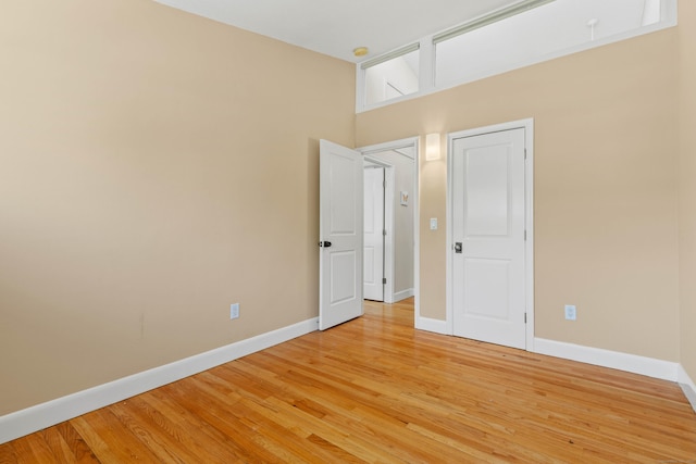 unfurnished room with a towering ceiling, baseboards, and light wood-style floors