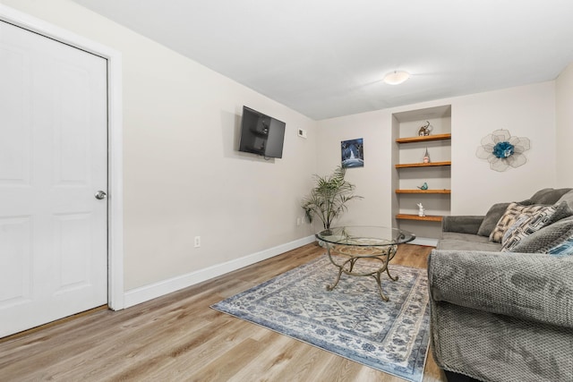 living room featuring built in shelves, baseboards, and wood finished floors