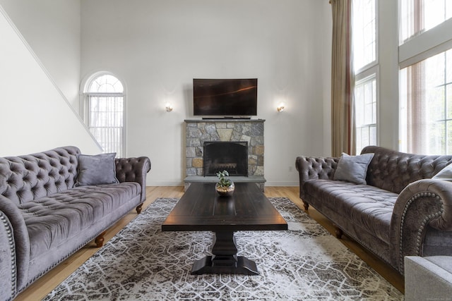 living area with a high ceiling, a fireplace, light wood-type flooring, and baseboards