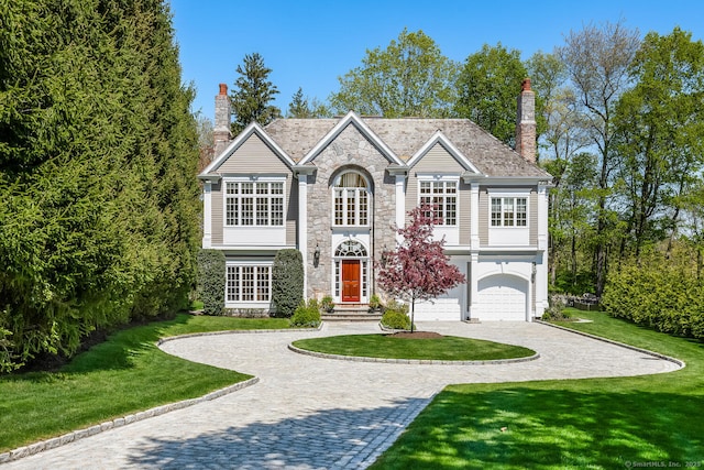 traditional home with a garage, a front lawn, stone siding, decorative driveway, and a chimney