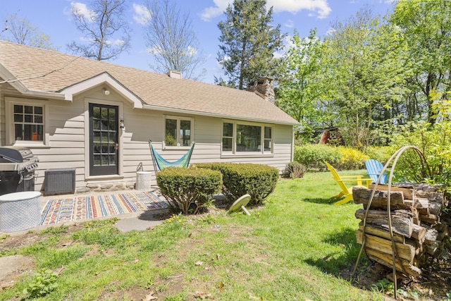 rear view of property featuring a lawn, roof with shingles, and a chimney