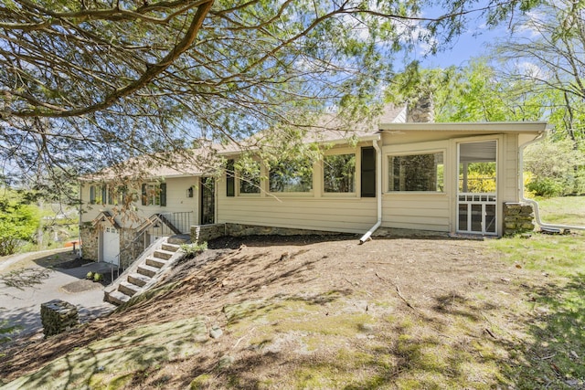 back of property featuring a chimney, stairs, stone siding, and a garage