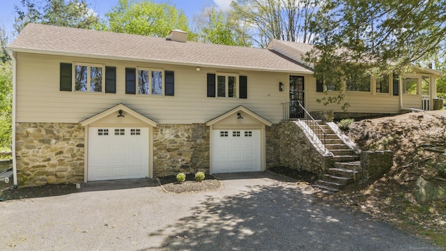 view of front facade with roof with shingles, an attached garage, aphalt driveway, and stone siding