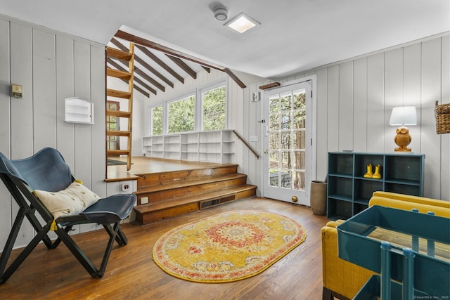 sitting room featuring visible vents, wooden walls, stairway, hardwood / wood-style flooring, and lofted ceiling with beams