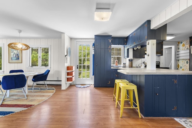 kitchen with blue cabinetry, light countertops, light wood finished floors, a peninsula, and a breakfast bar