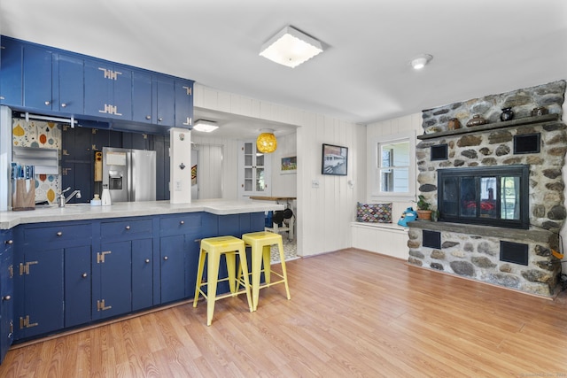 kitchen with light countertops, light wood-type flooring, a kitchen bar, stainless steel refrigerator with ice dispenser, and blue cabinets