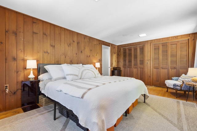 bedroom with multiple closets, wood walls, and light wood-style flooring
