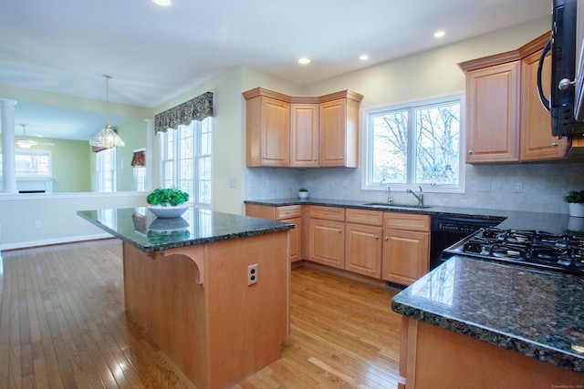 kitchen with black microwave, light wood finished floors, a breakfast bar area, a center island, and a healthy amount of sunlight