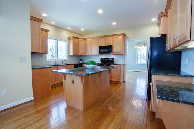 kitchen featuring light wood-style flooring, a center island, baseboards, backsplash, and black appliances