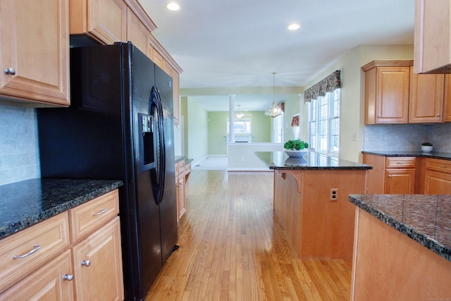 kitchen featuring black fridge with ice dispenser, dark stone counters, light wood finished floors, and backsplash