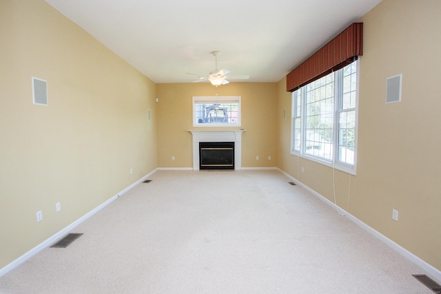 unfurnished living room with visible vents, a glass covered fireplace, and light colored carpet