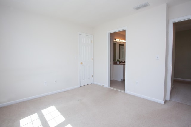 unfurnished bedroom with baseboards, ensuite bathroom, light carpet, and visible vents