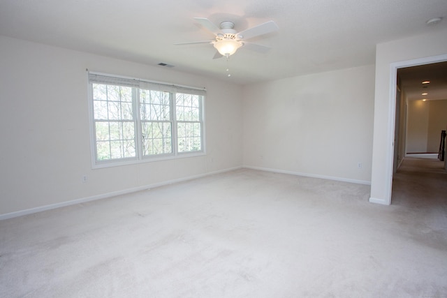 empty room with ceiling fan, light colored carpet, baseboards, and visible vents