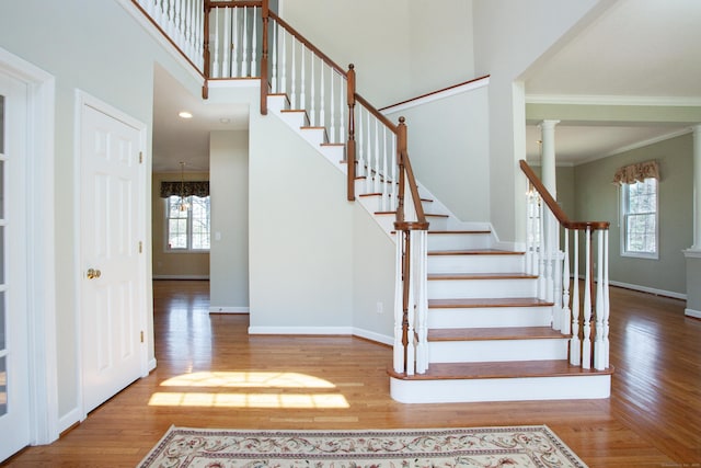 staircase featuring wood finished floors, a high ceiling, baseboards, an inviting chandelier, and ornamental molding