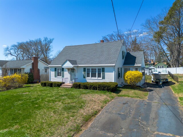 cape cod home featuring roof with shingles, fence, aphalt driveway, a front yard, and a chimney
