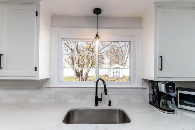 kitchen with decorative backsplash, pendant lighting, white cabinetry, stainless steel microwave, and a sink