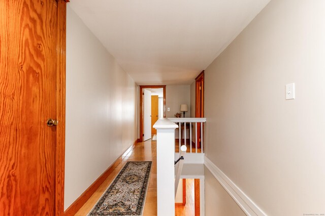 hallway with baseboards, light wood-style flooring, and an upstairs landing