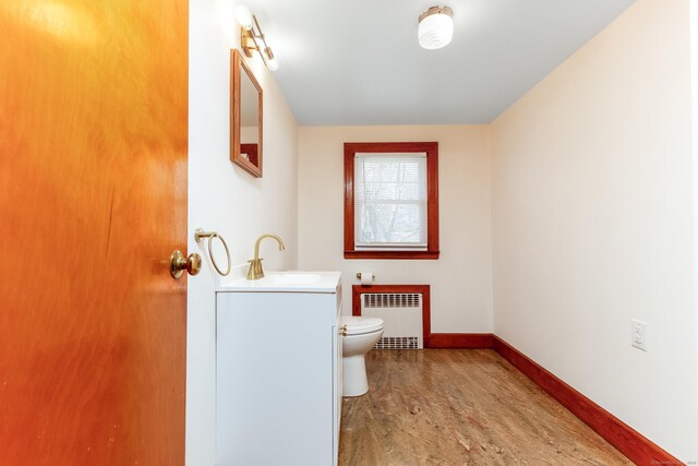 half bath with vanity, radiator, wood finished floors, toilet, and baseboards