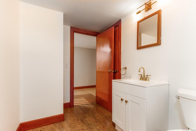 half bathroom featuring toilet, baseboards, and vanity